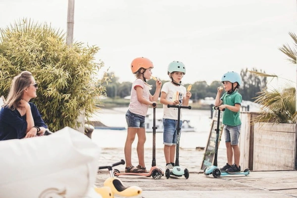 troje dzieci w kaskach i na hulajnogach Scoot And Ride zajada lody przy plaży